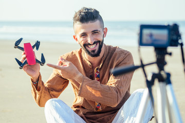 arabian man sitting on sand and talking tripod video making review of quadrocopter in beach. Travel...