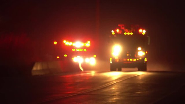 Emergency vehicles driving with lights flashing with ambulance following fire truck down road at night with sirens on.