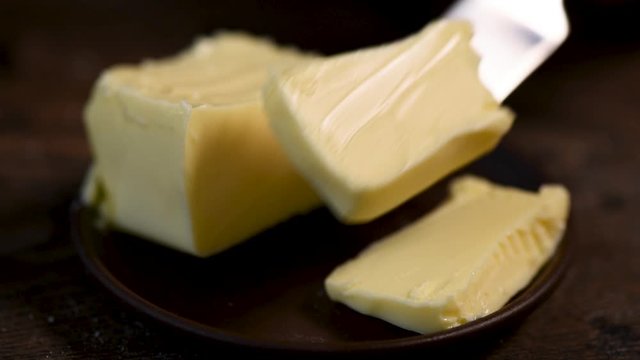 Taking cube of butter with a knife closeup view. Raw organic butter