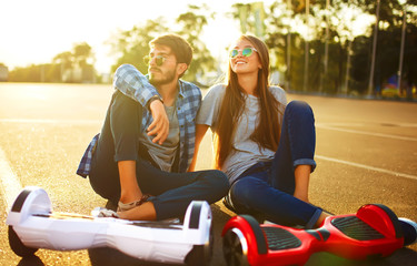 Happy man and woman riding on the Hoverboard for relaxing time together outdoor at the city. A young couple riding a hoverboard in a park, self-balancing scooter. Active lifestyle technology future.