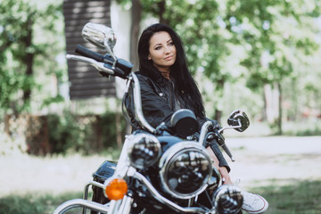 Fototapeta na wymiar Biker woman in a leather jacket on a motorcycle looks into the distance on a summer sunny day on a green background.