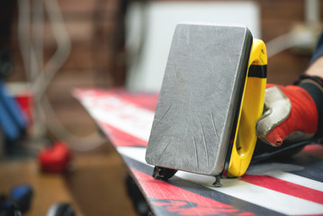 Fototapeta premium Worker is applying a wax on a slippery surface of snowboard by iron close up.