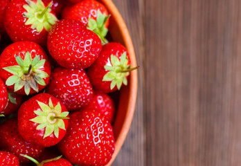 Red tasty strawberries in a clay plate on a wooden background. Freshly picked strawberries