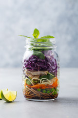 Healthy asian salad with noodles, vegetables, chicken and tofu in glass jars. Grey background.
