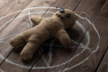 Voodoo doll on a wooden background with dramatic lighting. The concept of witchcraft and black art and the occult. Burlap doll on the background of a drawn star. Stuck pins in the doll.
