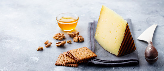 Hard cheese, Manchego with nuts, honey and crackers on grey background. Copy space.