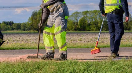 eine Ölspur auf der Straße wird von zwei Männern beseitigt