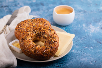 fresh bagels with butter and cheese on plate and cup of coffee on blue background