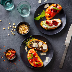 Bruschetta with tomatoes, cheese and olive tapenade on black plates. Slate background. Top view.