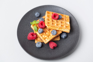 Belgian waffles with fresh berries and mint. Waffles with berries in plate on grey table. 