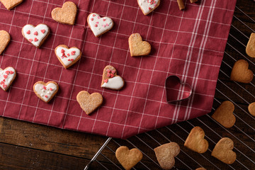 homemade cookies hearts with white icing and pastry topping on kitchen maroon towel and metal grate for Valentine's day