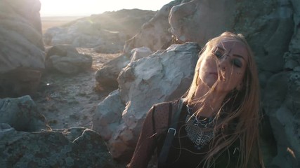 blond woman in a black ethnic occult dress moves in a trance dance among the mountain stones at sunset. Sensitive wind and with eyes closed. minimalistic black style and occultism - Powered by Adobe