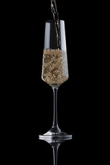 Golden champagne pours into a transparent luxury elegant glass isolated on black background. Sparkling wine with bubbles fills the glass