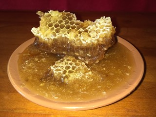 golden yellow hexagonal honeycombs in a clay brown plate on a wooden background