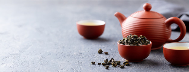 Green tea oolong in a clay tea cup bowl and tea pot. Stone background. Copy space.