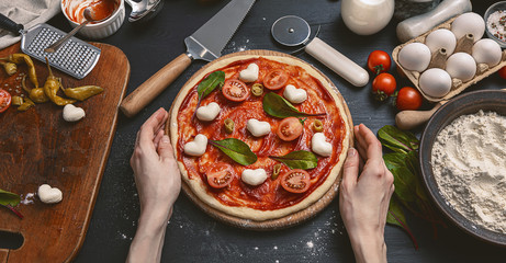 Classic pizza margherita with heart-shaped mazarella cheese. preparing a phased gala dinner for two at home in honor of Valentine's Day.