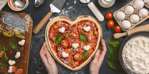 woman preparing a festive dinner for two in honor of Valentine's Day classic Italian pizza Margherita in the shape of a heart and mozzarella in the shape of a heart