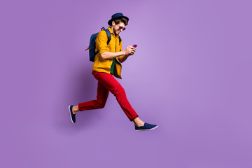 Plakat Full size profile side photo of positive hipster guy relax trip jump use smartphone search discounts run fast wear yellow shirt red pants rucksack isolated violet color background