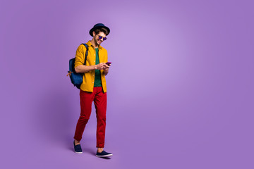 Full length profile side photo of positive guy hipster use smartphone go walk read social network blog news wear yellow shirt red pants bag velvet headwear isolated vibrant color background