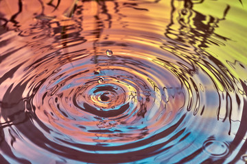 Raindrops fall on the surface of the water. The circles from the raindrops on the water surface. Abstract color background of circles on the water and falling drops.