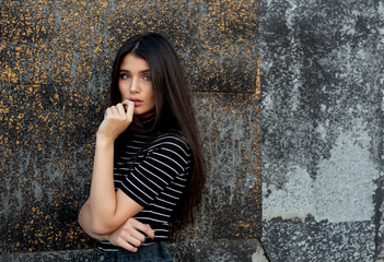 Beauty portrait of a sensual girl with straight brunette hair, dressed in modern clothes, with makeup, supported by a black wall.