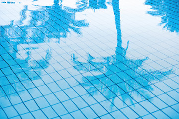 Tropical background of palm trees leaves reflection in the blue calm water surface of a luxury hotel pool. Abstract background with openwork outline of palm leaves. Holiday vacation concept.