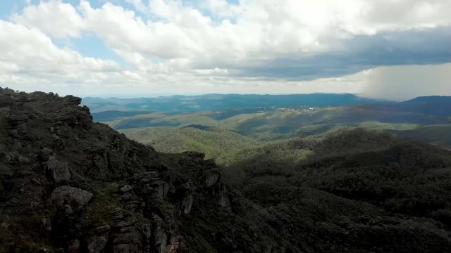 Rocky cliffs in shadow against a blue sky with clouds on the left turning towards heavy rainfall over the Minas Gerais rolling hills on the right seen from the Itacolomi trail in Ouro Preto, Brazil