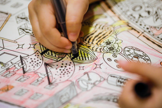 Shallow Depth Of Field (selective Focus) And Macro Image With The Hand Of A Little Girl Using A Sharpie To Draw On A Coloring Book.