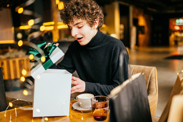 Shocked man opening present boxes at Christmas. Excited bearded guy holds gift with opened mouth. Christmas gifts time. Man enjoying christmas holidays at home.