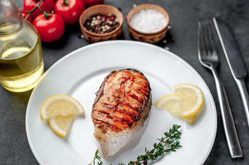 Grilled salmon steak in a white plate with spices, fork and knife on a stone background
