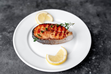 Grilled salmon steak in a white plate with spices on a stone background