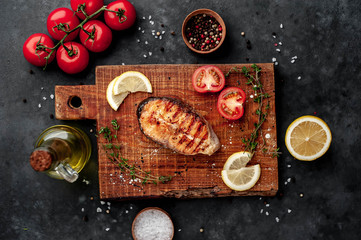 Three grilled salmon steaks with spices, lemon and tomatoes on a stone background