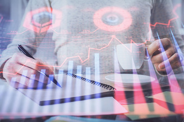 Forex chart hologram on hand taking notes background. Concept of analysis. Double exposure