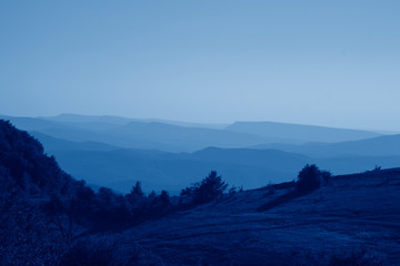 Scenic views of mountain landscape, rocks and valley in summer toned in trendy Classic Blue color of the Year 2020.  Beautiful minimalist landscape of mountain ranges covered with forest.