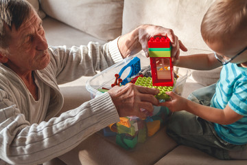 Elderly grandpa or grandfather plays with his little grandson