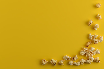  A scattering of popcorn in the lower corner on yellow background. Copy space, flat lay. Close-Up Of Popcorn Against Yellow Background.
