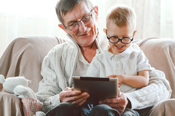 Elderly grandfather and his little grandson use a tablet device