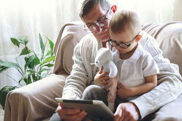 Elderly grandfather and his little grandson use a tablet device