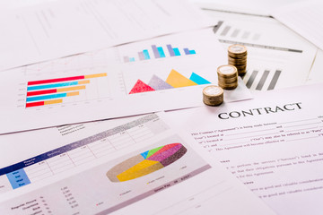 Coins stacked on documents of an economic contract.