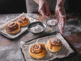 Female hands sprinkle powdered sugar with fresh sweet homemade cinnamon rolls and chocolate cream....