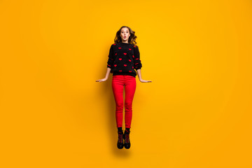 Obraz premium Full length photo of funny lady jumping up high spending free time weekend rejoicing wear hearts pattern sweater red trousers footwear isolated yellow color background