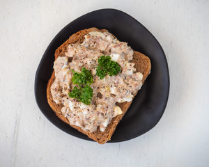 Sandwich on dark bread with saury salad and chicken eggs on a white table