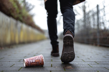 Mann wirft leeren Kaffeebecher auf Gehweg