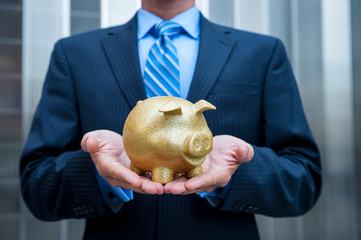 Unrecognizable businessman holding a sparkly gold piggy bank outside a modern metallic office building background
