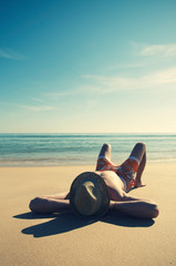 Fototapeta na wymiar Silhouette of a unrecognizable man wearing a straw sun hat relaxing on the smooth sand of an empty beach