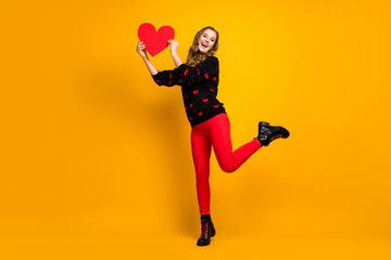 Fototapeta na wymiar I catch you. Full length photo of pretty lady hold paper heart creative date invitation boyfriend wear hearts pattern sweater red pants shoes isolated yellow color background