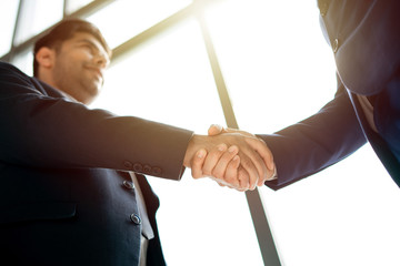 two businessman shaking hands at meeting room in office with glowing sun light