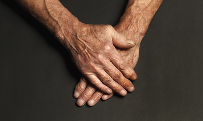 Wrinkled hands of an elderly man on a table close-up on a black