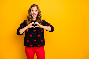 Naklejka premium Photo of excited funny curly lady inviting boyfriend romantic date showing arms heart shape figure wear black red hearts pattern sweater trousers isolated yellow color background