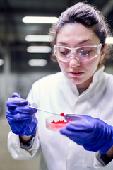 Young laboratory woman in glasses and petri dish in her hands is conducting experiments on defocused background